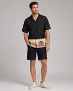 Man wearing a black shirt with a patterned waistband and dark shorts on a gray background