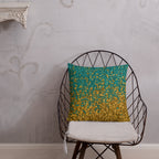 Decorative pillow with gold and green pattern on a black wire chair against a gray wall.