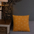 Orange patterned pillow on a gray sofa with a lamp and decorative fabric in the background.