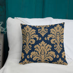 Decorative pillow with gold damask pattern on a blue background, placed on a white surface.