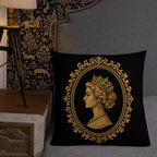 Decorative pillow with a gold emblem featuring a profile of a woman wearing a crown on a black background, placed on a gray sofa.