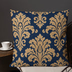 Decorative pillow with gold floral pattern on a blue background, placed on a chair next to a small table with a cup.